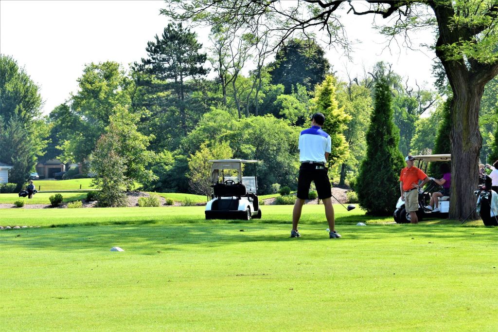 Golfer taking a swing with golfers and golf cart in distance
